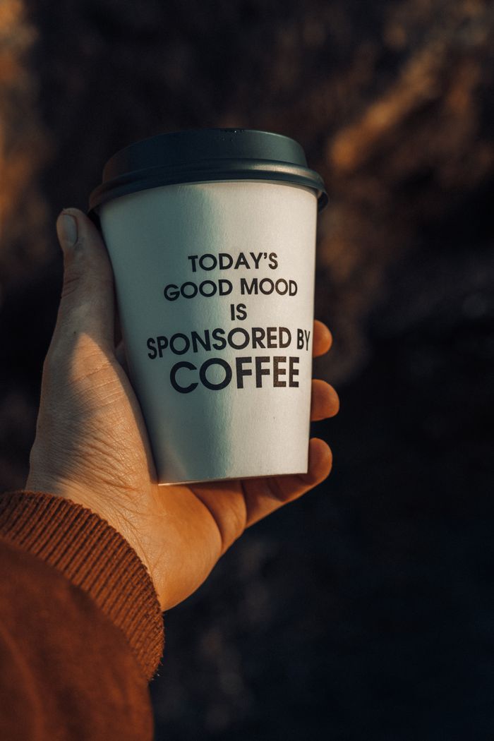About A hand holding a paper cup of coffee with a motivational quote outdoors.